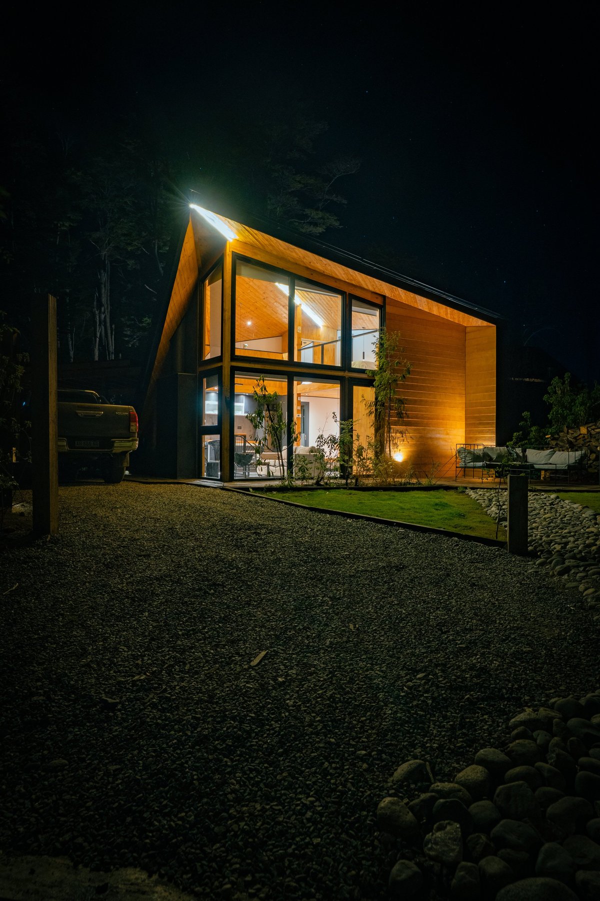 Modern luxury home warmly illuminated at twilight, surrounded by trees