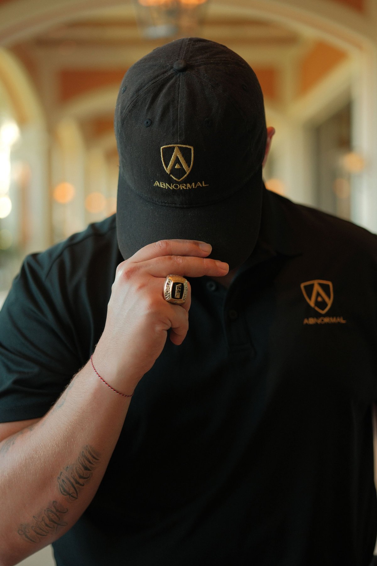 Member of the ABNORMAL team wearing the brand's black cap and shirt, displaying a gold ring and bracelet